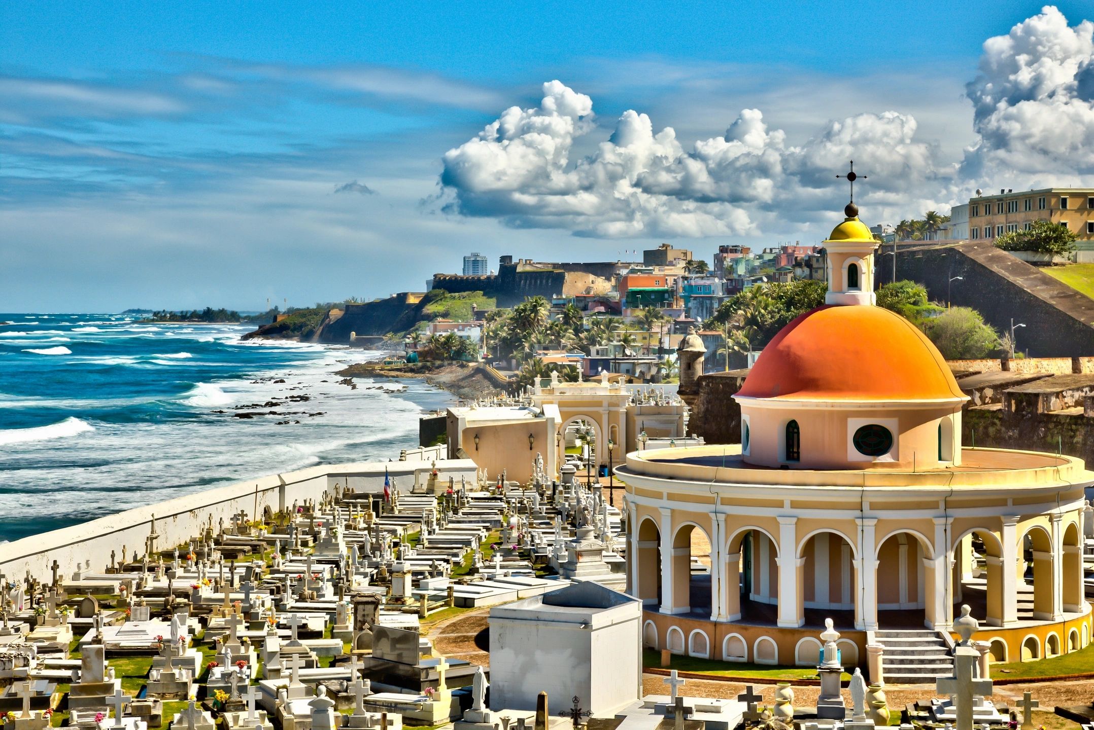 Colorful dome overlooking a seaside cemetery with vibrant buildings and blue sky.