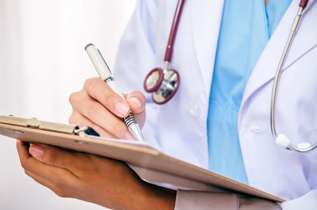 Doctor writing notes on a clipboard with a stethoscope around the neck.