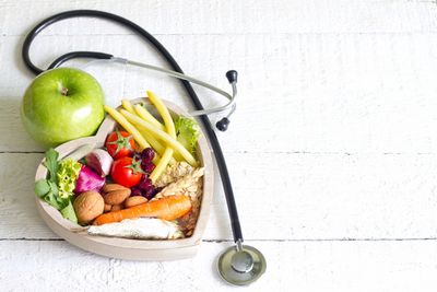 Green apple placed on top of a heart-shaped bowl full of vegetables and grain and a stethoscope next