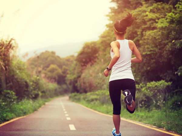 Woman jogging on a scenic forest road during sunrise.