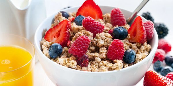 A bowl of granola with fresh berries and a glass of orange juice.