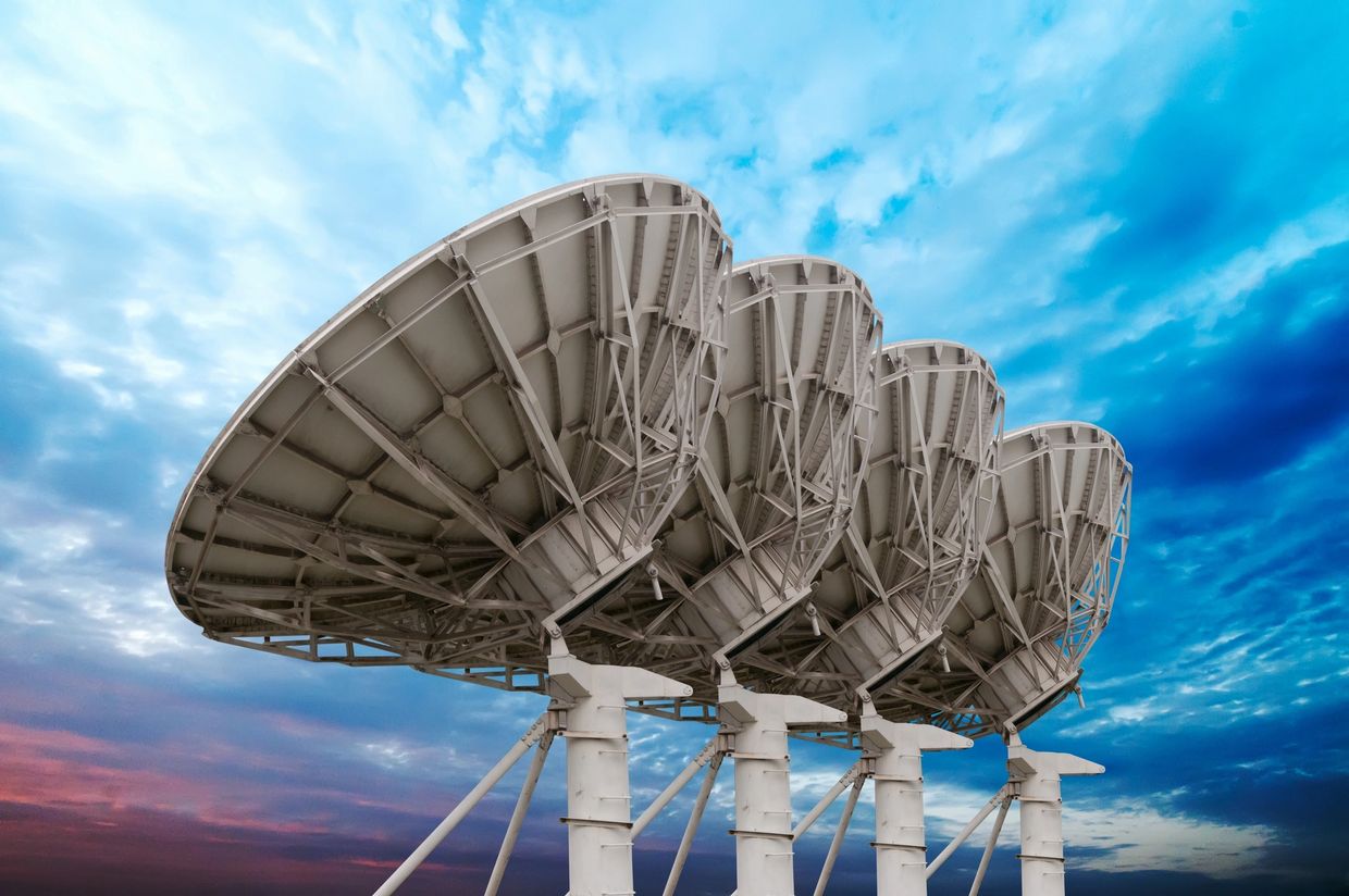 Four large satellite dishes under a vibrant sky.