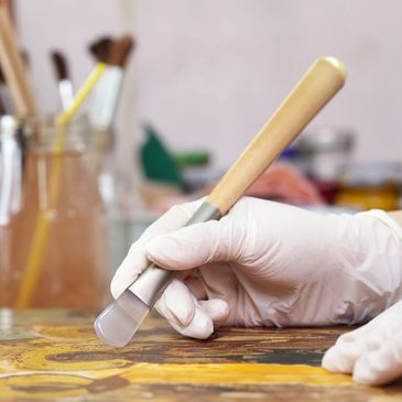 Gloved hand using a brush for art restoration on an old painting.