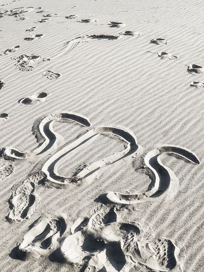 SOS written in the sand with footprints around it on a beach.