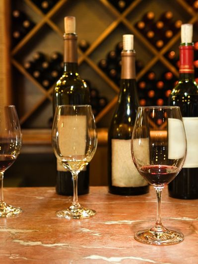 Wine bottles and glasses on a marble countertop with a wine rack in the background.