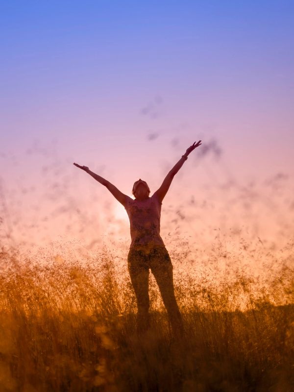 Silhouette of a person with arms raised in a golden field at sunset.