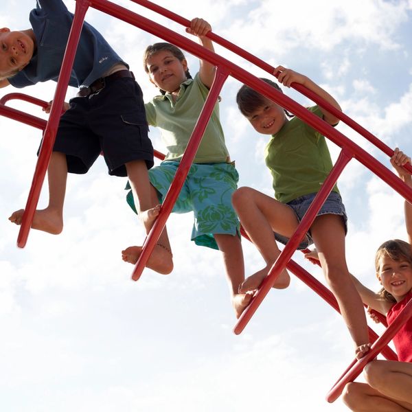 Children happily climbing a red jungle gym against a bright sky.