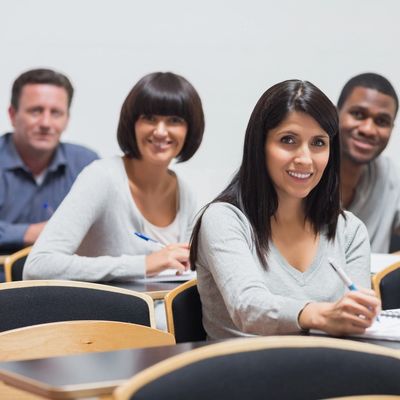 Diverse adult students smiling while sitting in a classroom with notebooks.