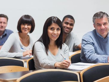 Adult students smiling while sitting in a classroom taking notes.They are attending Spoken English course for Advance English Communication Skills.