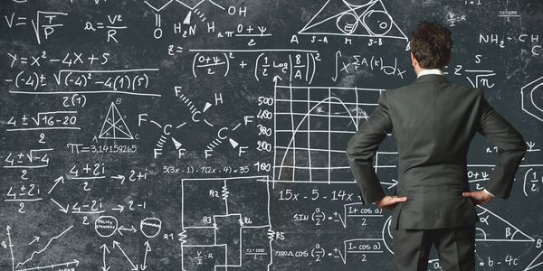 Man in suit solves complex formulas on chalkboard.