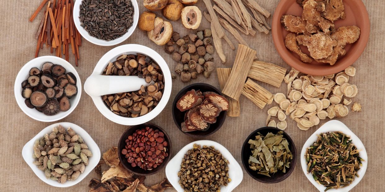 Various dried herbs and roots in bowls on a brown surface.