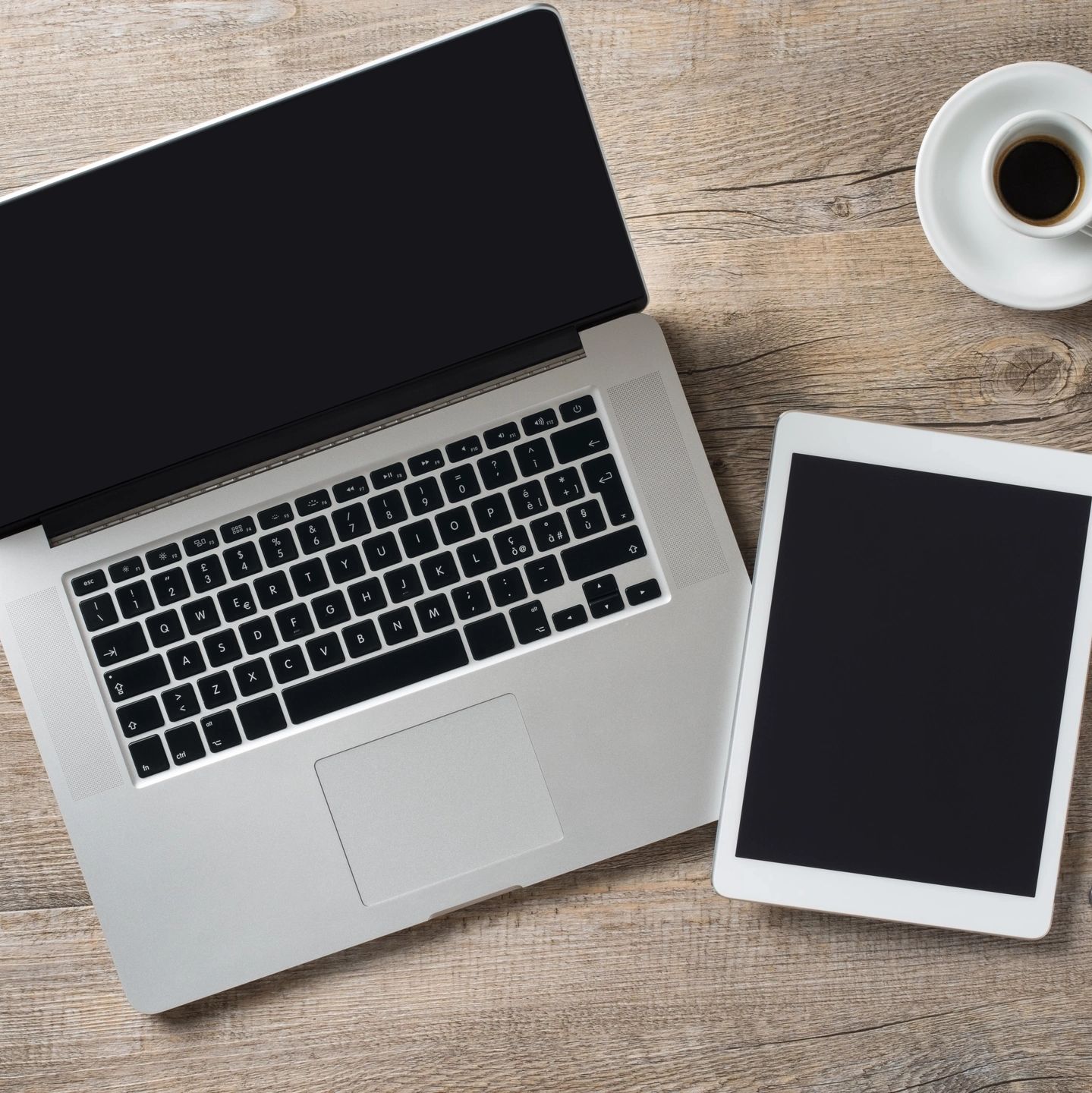 Laptop, tablet, and coffee cup on a wooden desk.