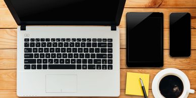 laptop computer, notebook, and mobile phone arranged on a desk with notepad and a cup of coffee - a 