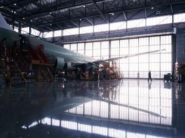 A large airplane inside a spacious, well-lit hangar with maintenance platforms.
