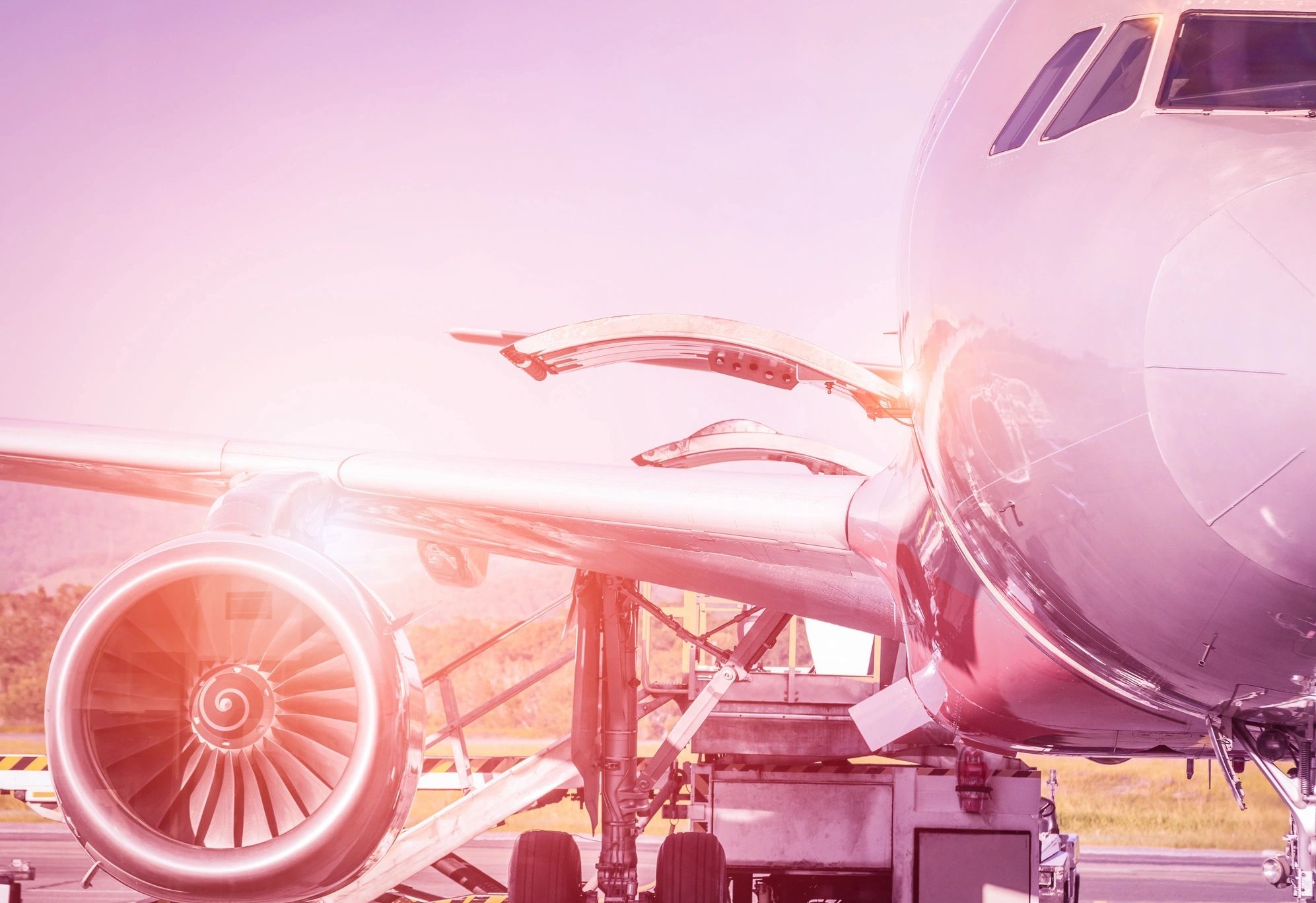 Close-up of a commercial airplane engine and wing with a pinkish filter.