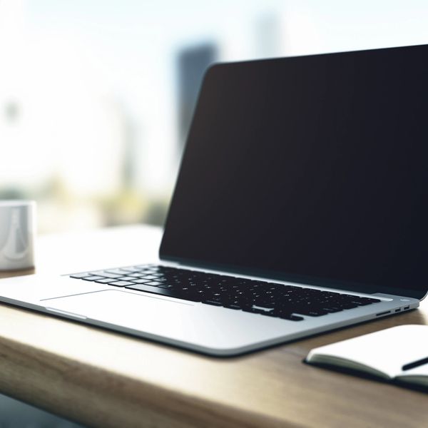 A closed laptop on a wooden desk with a cup and notebook nearby.