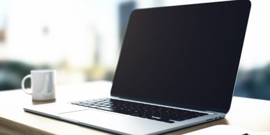 Laptop on desk with white mug to the left and a bright window in the background