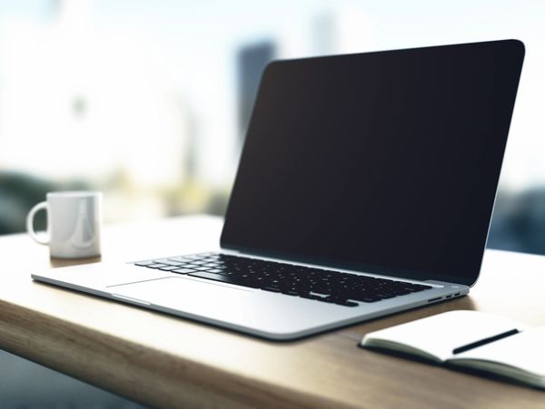 Laptop on a wooden desk with a coffee mug and notebook.