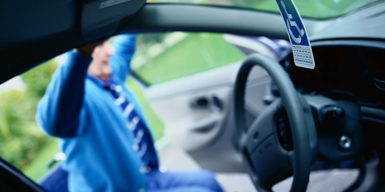 Handicap permit hanging in car with elderly person entering.