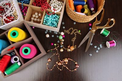 Colorful beads, threads, and scissors arranged for jewelry making on a wooden table.
