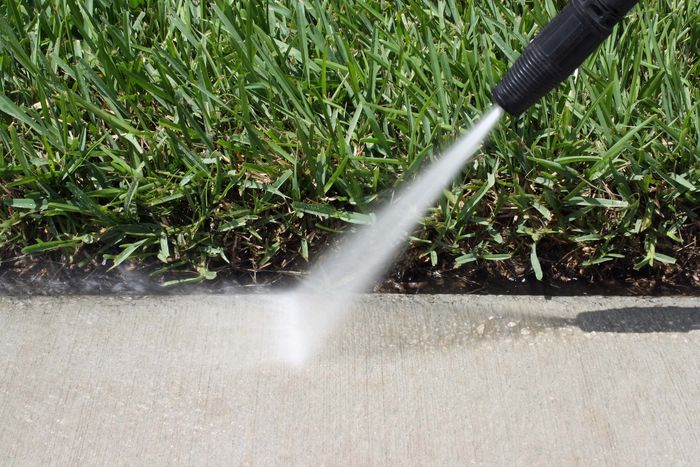 Pressure washing a concrete sidewalk next to grass.