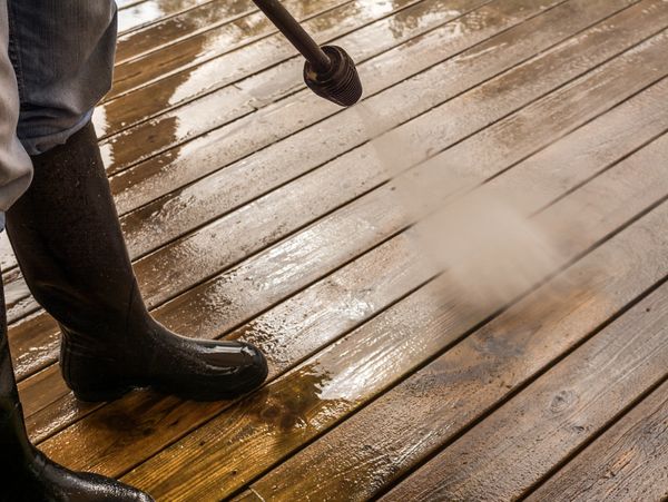 Person pressure washing a wooden deck wearing black boots.