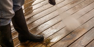 person pressure washing a wooden deck wearing water boots