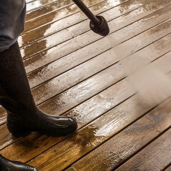 Person cleaning a wooden deck with a pressure washer.