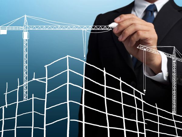 Businessman drawing a construction plan with cranes and building outlines.