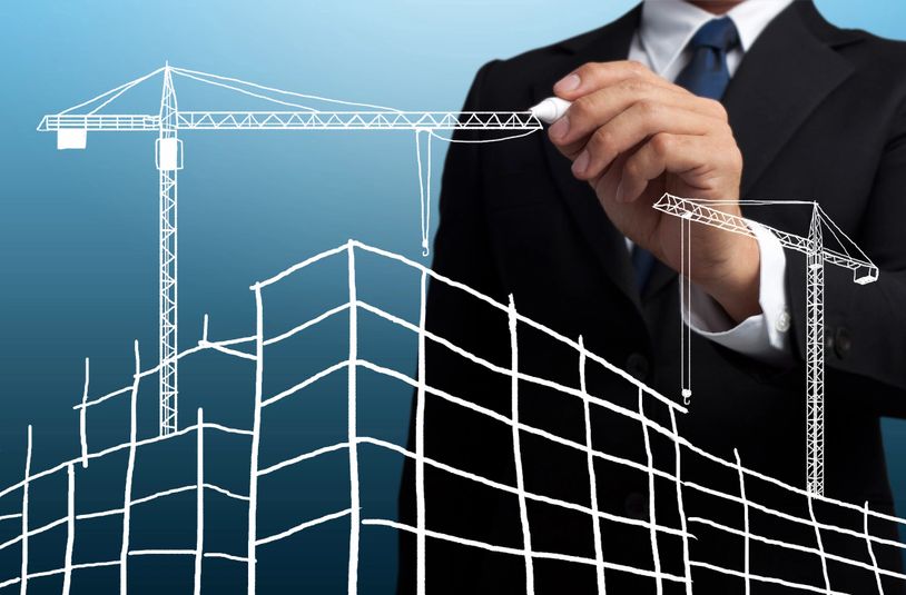 A businessman drawing construction cranes and building outlines on a transparent screen.