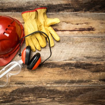 A hard hat, ear protection, gloves and goggles are on a wood table.