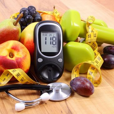 Glucometer with fresh fruits, dumbbells, and stethoscope symbolizing health and fitness.