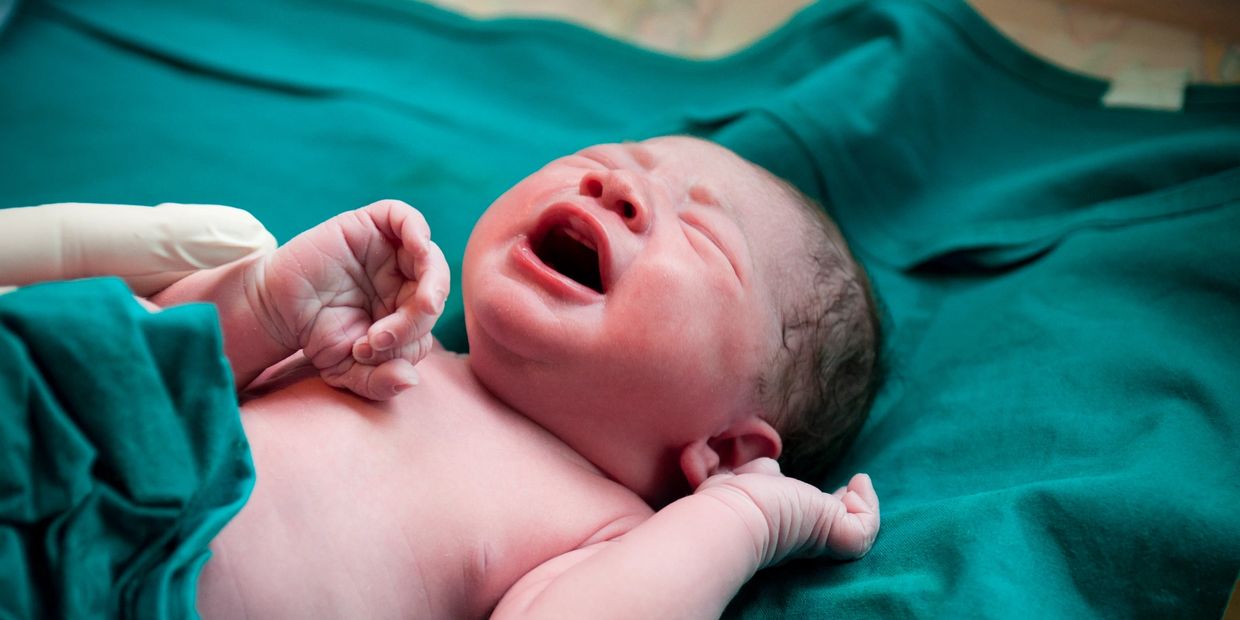 Newborn baby crying on green hospital blanket