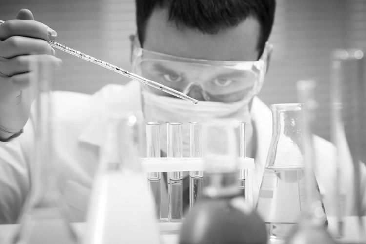 Scientist carefully drops blue liquid into test tubes in lab.