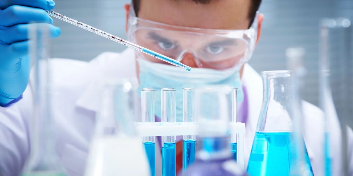 Scientist drops blue liquid into test tube in lab.