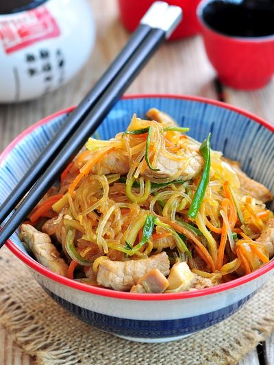 Bowl of stir-fried noodles with vegetables and meat.