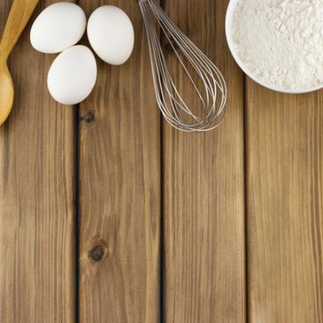 Eggs, flour, and a whisk on a wooden surface for baking.
