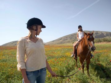 Woman leading a horse with a rider in a field.