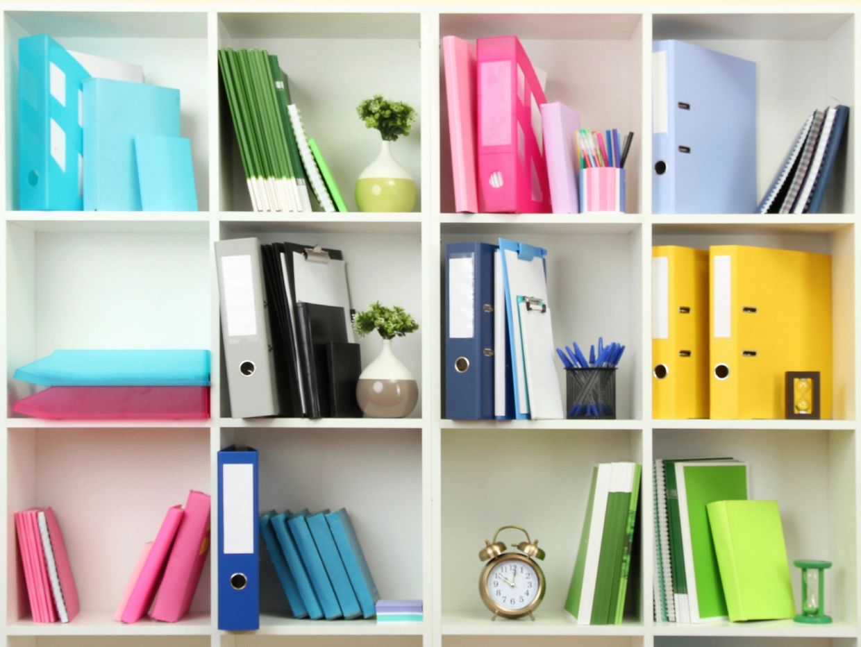Organized shelves with colorful folders, notebooks, and decorative plants.