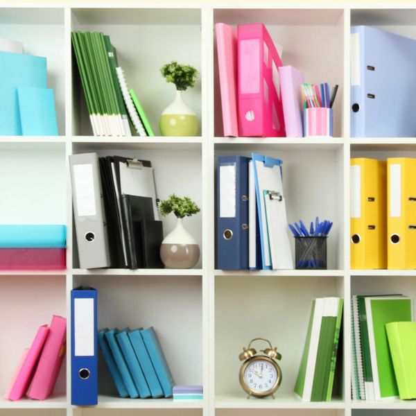 Organized colorful binders, books, and office supplies on white shelves.