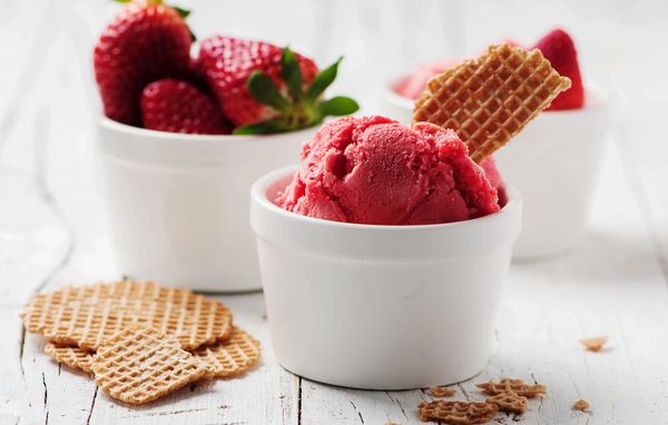 A scoop of strawberry sorbet with a waffle cookie in a white cup.
