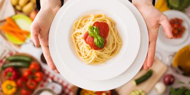 A plate of spaghetti with tomato sauce and basil held by hands.