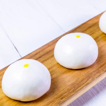 Three round steamed buns with a yellow dot on top on a wooden platter.