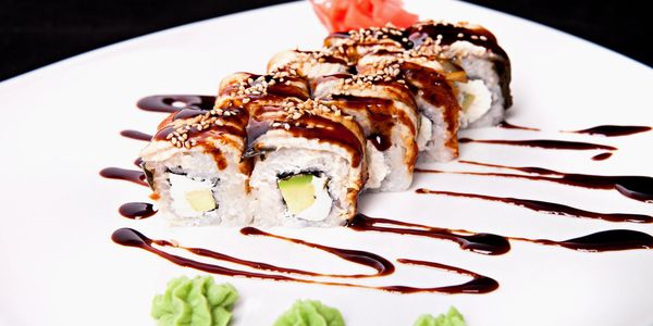 Sushi rolls drizzled with sauce and topped with sesame seeds on a white plate.