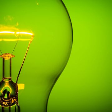 Close-up of a glowing light bulb filament against a green background.