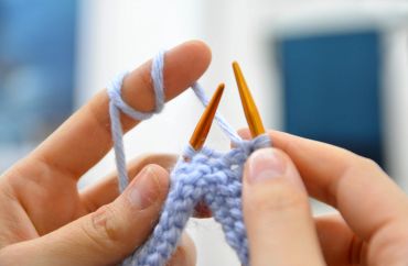 Hands knitting with blue yarn on wooden needles.