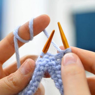 Close-up of hands knitting with light blue yarn and orange needles.