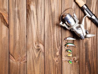Fishing rod and various colorful fishing lures on wooden background.