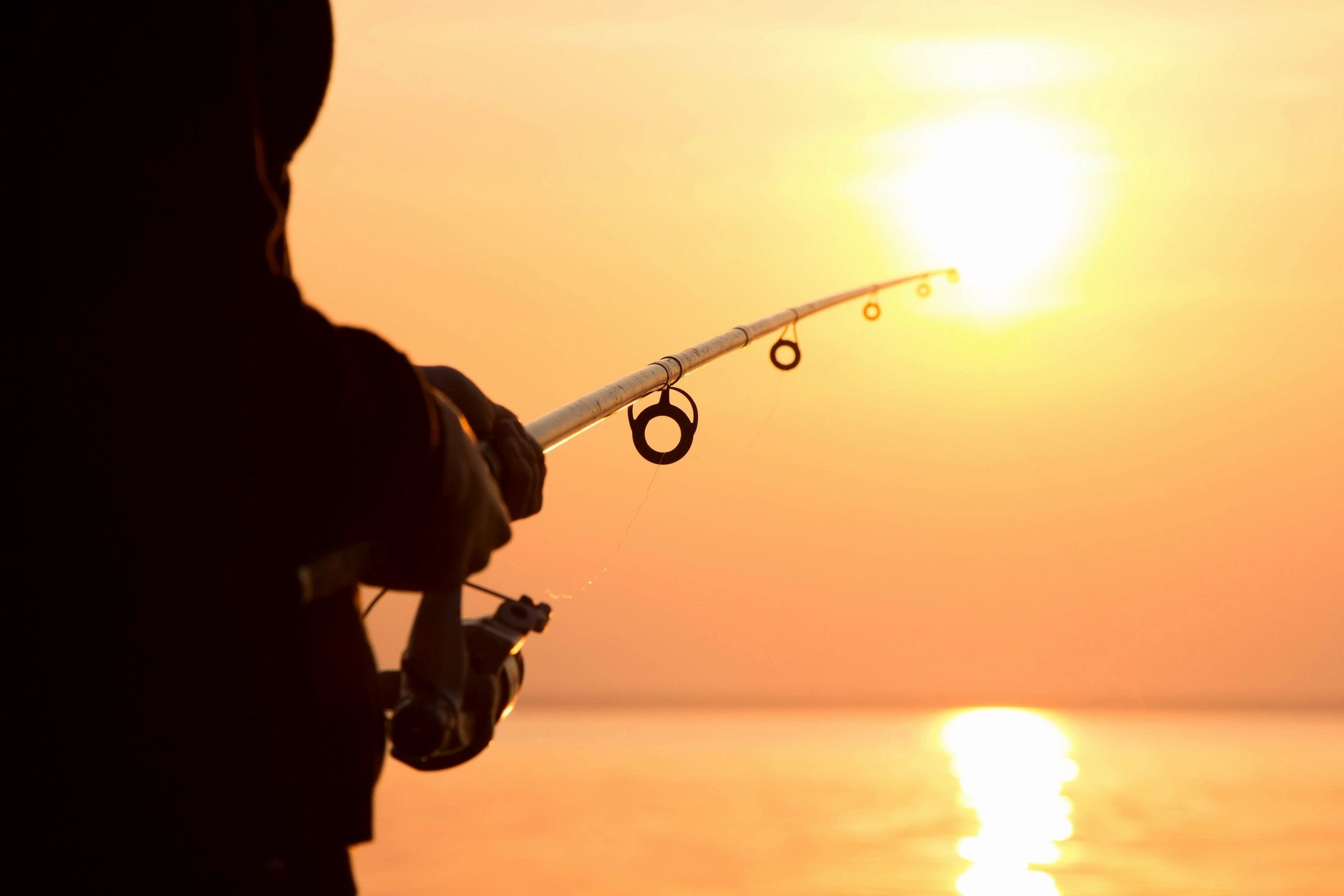 Angler fishing on a lake under the sunset at dusk.