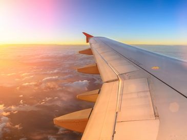 View of an airplane wing flying above clouds at sunrise.